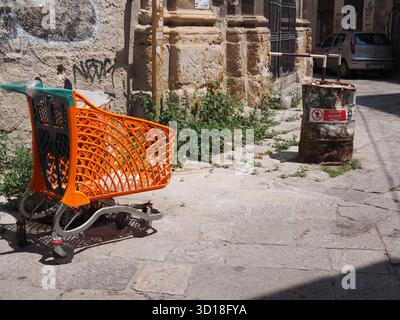 Chariot abandonné et tonneau rouillé dans une rue étroite de Palerme, Sicile, Italie, entouré de graffitis et de vieux murs de pierre Banque D'Images