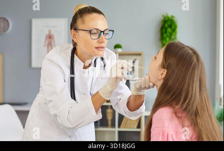 Le pédiatre prélève le prélèvement d'un écouvillon de gorge chez un enfant au cours d'un examen en clinique Banque D'Images