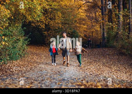 Père se tenant la main avec ses deux enfants pendant la marche d'automne. Banque D'Images