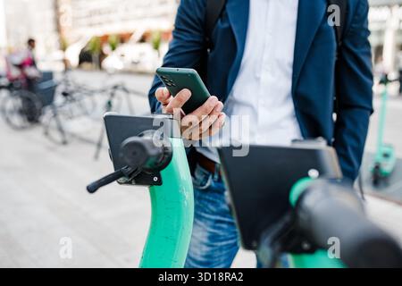 Homme d'affaires déverrouillant scooter électrique avec smartphone. Banque D'Images