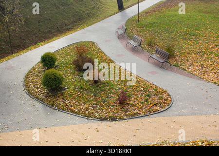 Vue d'automne d'un parterre de fleurs entre les chemins dans un parc de la ville. Bancs vides dans un parc d'automne. Les ruelles sont parsemées de feuilles jaunes tombées. Automne en t Banque D'Images