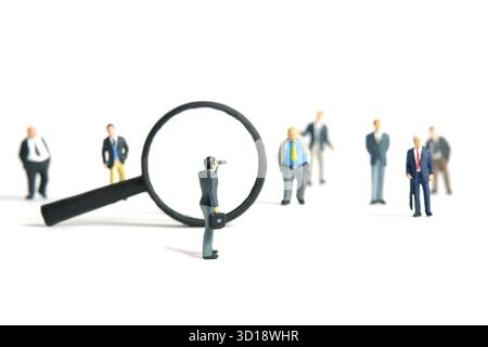 Photographie miniature de personnages jouet. Un homme d'affaires utilisant binoculaire trouver candidat debout devant la loupe. Isolé sur un bac blanc Banque D'Images