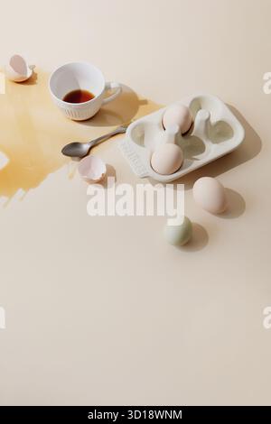 Œufs et tasse à café renversée. Café renversé et œufs sur table beige, concept de photographie alimentaire créative avec coquilles d'œufs cassées Banque D'Images