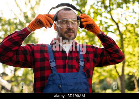 Travailleur dans le jardin uniforme ajustant l'équipement de protection auditive Banque D'Images