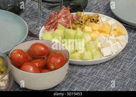 Table avec en-cas légers. Fromage en dés, olives, bacon, fromage feta, fruits sucrés, tomates marinées Banque D'Images