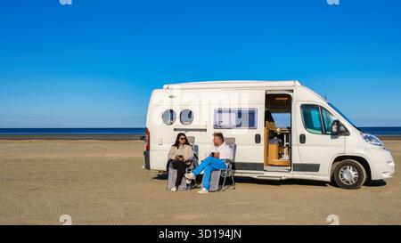 Un couple est assis ensemble devant un camping-car Van sur les dunes douces, entouré d'herbes hautes, regardant les vagues calmes de la mer du Nord pendant l'heure d'or à Blokhus Strand, Danemark Banque D'Images