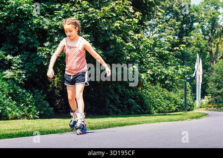 Fille sur patins à roulettes. Fille de 8-10 ans apprenant à patiner dans un parc d'été Banque D'Images