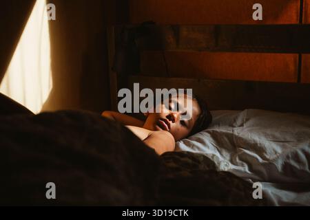 Enfant dormant paisiblement dans son lit tandis que la lumière chaude du matin filtre à travers une fenêtre, projetant une lueur sereine. L'atmosphère est calme et reposante, réfléchissante Banque D'Images