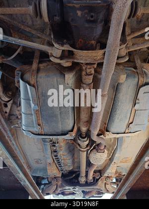 Vue de bas en haut du dessous ou du train de roulement rouillé d'une vieille voiture. Composants de suspension et d'échappement rouillés sous la carrosserie, vue grand angle, personne Banque D'Images