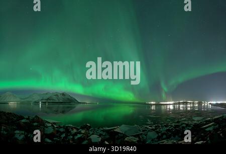 Vue de l'aurore boréale verte éthérée dansant à travers le ciel sombre, reflétée dans les eaux calmes près de la rive rocheuse, Reykjavík, Reykjavíkurborg, Banque D'Images