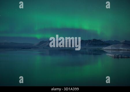 Vue sur les danses vertes éthérées d'aurora borealis au-dessus du lagon glacé, reflétant dans les eaux calmes sous les montagnes enneigées, Jokulsarlon, Banque D'Images