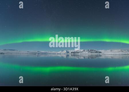 Vue des aurores boréales vertes éthérées dansant au-dessus des eaux sereines réfléchissantes, reflétant l'exposition céleste, Jokulsarlon, Sveitarfélagið Hornafjörður, Islande. Banque D'Images