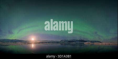 Vue sur les aurores boréales vertes éthérées dansant au-dessus des eaux tranquilles reflétant la douce lueur de la lune, Jokulsarlon, Sveitarfélagið Hornafjörður, Islande. Banque D'Images
