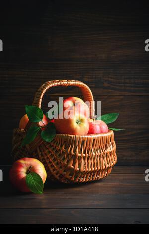 Pommes mûres dans un panier en osier sur un fond en bois Banque D'Images