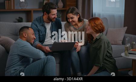 Quatre amis ethniques de diversité avec ordinateur portable souriant heureux communiquer à la maison partie multiraciale personnes insouciantes discutant de choisir le film Internet en ligne Banque D'Images