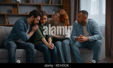 Quatre personnes multiraciales partie à la maison frustré femme amis soutenant calmer sur le canapé ensemble bouleversé la fille tenant la tête parler problème rupture Banque D'Images