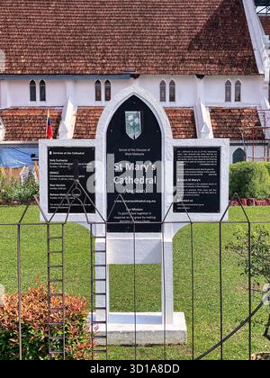 Cathédrale anglicane Sainte-Marie, Kuala Lumpur, Malaisie. Le bâtiment historique de l'église avec son toit carrelé distinctif, ses murs blancs, et un panneau d'information proéminent sur une pelouse verte Banque D'Images