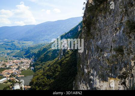 Vue aérienne d'une falaise spectaculaire plongeant dans une vallée avec une petite ville nichée au-dessous des montagnes verdoyantes, Salorno, Trentin-Haut-Adige, Italie. Banque D'Images