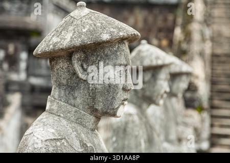 Des statues en pierre de gardes royaux se dressent dans une rangée avec les mains pliées, portant des vêtements traditionnels vietnamiens et des chapeaux au Tombeau de Khai Dinh à Hue, au Vietnam, symbolisant l'autorité impériale et l'honneur cérémoniel Banque D'Images
