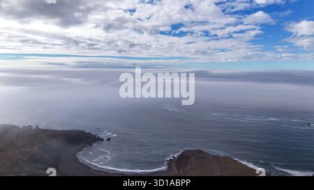 Vue aérienne de la rencontre de la terre, de la mer et du ciel où l'horizon brumeux brouille la ligne entre l'eau et l'atmosphère, créant une scène côtière sereine et éthéré. Banque D'Images