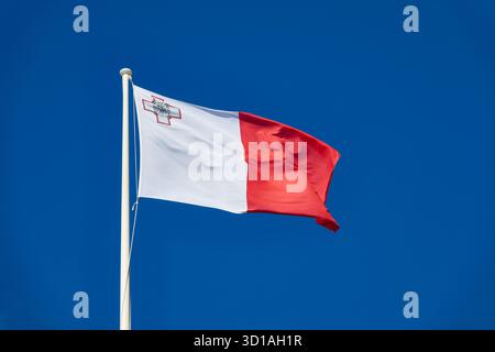 Drapeau maltais volant contre ciel bleu clair avec l'emblème de la croix maltaise à l'élévateur Banque D'Images