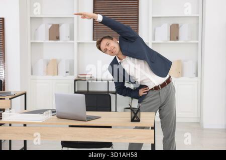 Jeune homme d'affaires faisant l'exercice d'étirement dans le bureau Banque D'Images