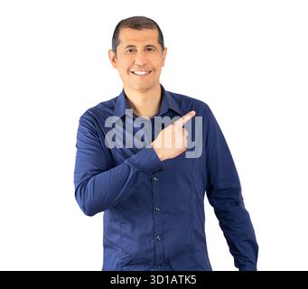 Bel homme hispanique portant une chemise bleue décontractée sur fond blanc. Surpris pointant avec le doigt sur le côté, bouche ouverte expression étonnée. Banque D'Images