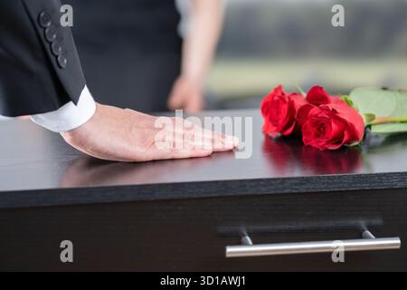 Mort, funérailles et main d'homme sur cercueil, famille au service dans le cimetière ou l'église pour le respect. Fleurs, perte et les gens au cercueil en bois dans le cimetière wi Banque D'Images