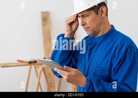 Travailleur de la construction inquiet vérifiant la tablette dans un bâtiment Banque D'Images