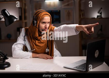 Médecin musulman en colère portant le hijab et le stéthoscope criant et pointant vers vous tout en travaillant sur le quart de nuit à l'hôpital. Médecine de la santé c Banque D'Images