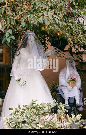 Les squelettes habillés en mariée et mariée posent dans un jardin, créant une décoration ludique pour Halloween. Banque D'Images
