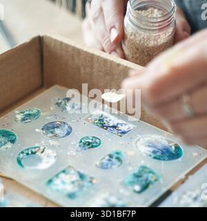 Mains fabriquant des bijoux en résine colorés à l'aide de moules et d'embellissements. Banque D'Images