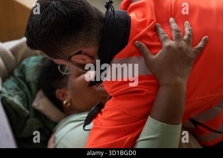 Femme noire d'âge moyen allongée sur le canapé aidée par un jeune adulte homme caucasien ambulant en uniforme, ambulant penché sur la fourniture de soins médicaux d'urgence Banque D'Images