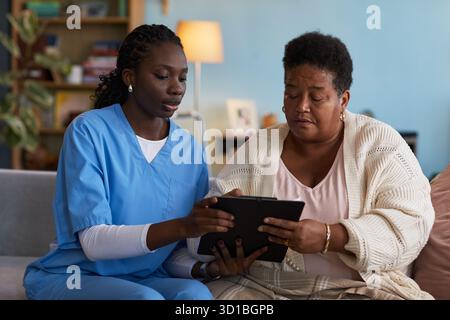 Jeune femme noire infirmière portant des gommages médicaux aidant femme noire d'âge moyen remplissant des documents sur presse-papiers, les deux se concentrant sur les documents, professionnel de la santé soutenant le patient Banque D'Images