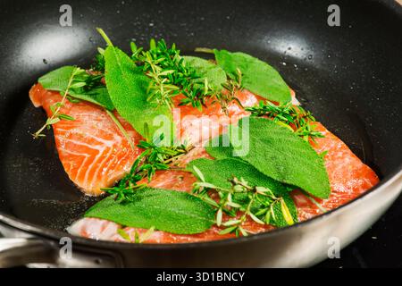 Vue surélevée de deux filets de saumon marinés avec de la sauge fraîche et du thym dans une poêle à frire enduite de noir. Banque D'Images