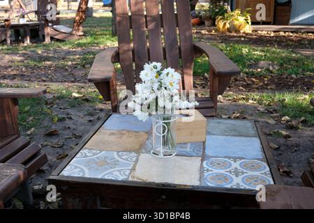Un cadre de jardin confortable dispose d'une table avec des fleurs et des chaises en bois à proximité. Banque D'Images