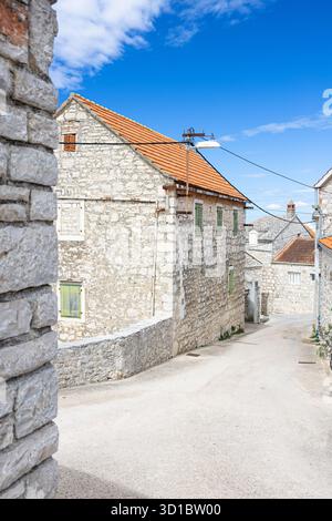 De pittoresques maisons en pierre bordent une étroite rue ensoleillée dans un village côtier. Les toits en tuiles rouges, les volets verts et le ciel bleu clair créent un charme, salut Banque D'Images