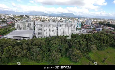 Vue aérienne des bâtiments résidentiels entourés d'arbres, avec vue sur la montagne et le ciel bleu à Joinville, Brésil. Banque D'Images