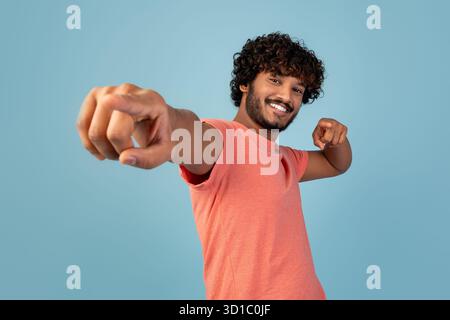 Attrayant jeune homme indien pointant la caméra et souriant sur fond bleu Banque D'Images