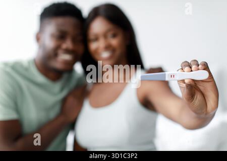 Un couple excité partage un moment joyeux avec un test de grossesse positif dans un cadre confortable à la maison Banque D'Images