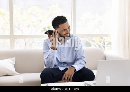 Heureux homme africain tient smartphone près de l'oreille écoutant le message audio Banque D'Images