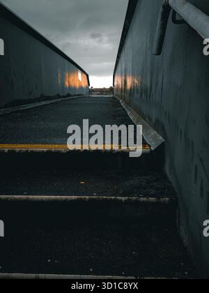 Une vue spectaculaire en perspective profonde et à faible angle d'un escalier sombre et raide menant à un passage supérieur ou inférieur urbain clos. Le brut, peint en noir Banque D'Images