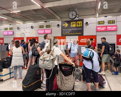 Les personnes qui attendent avec des bagages à un terminal d'aéroport près des panneaux de porte et une horloge dans la zone d'embarquement Banque D'Images