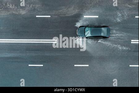 la voiture roule vite avec des pulvérisations sur une route inondée après une averse. vue aérienne de dessus depuis un drone volant. Banque D'Images