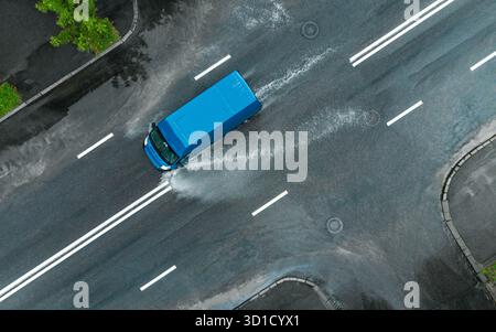 blue van conduit rapidement sur une route humide inondée. éclaboussures d'eau sous les roues d'une voiture. vue aérienne de dessus. Banque D'Images