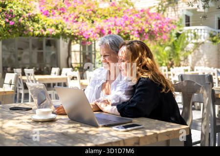 Deux femmes matures appréciant le travail à distance ensemble sur des ordinateurs portables à Outdoor Cafe le jour ensoleillé de l'été Banque D'Images