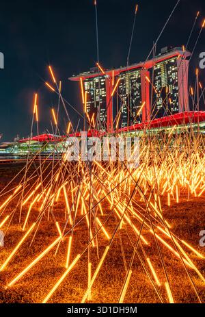 Installation lumineuse avec des tiges LED la nuit, avec Marina Bay Sands à Singapour comme toile de fond de ville dynamique. Banque D'Images