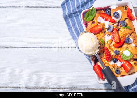 Tarte parée aux petits fruits d'été, gâteau maison avec myrtille sucrée et fraise, servi avec boule de glace à la vanille, sur bois blanc ensoleillé Banque D'Images