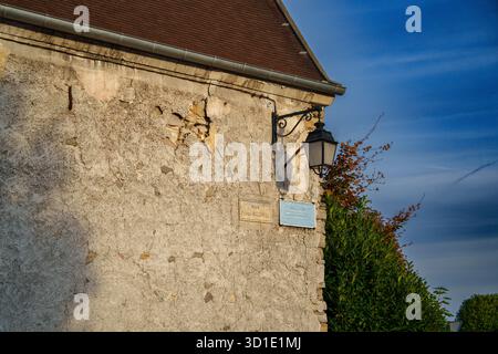 Une vue rapprochée d'un mur de pierre texturé dans un village français, avec un lampadaire vintage et une signalisation informative, baigné dans la lumière chaude d'un soleil Banque D'Images