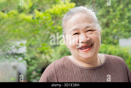 Femme âgée joyeuse debout dans le jardin à la maison, souriant avec des dents blanches parfaites, riant, geste, jouissant de loisirs, confort, amuse-toi bien Banque D'Images
